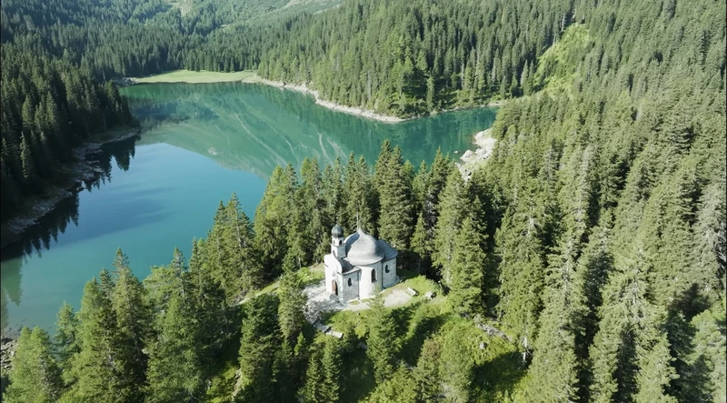 Standbild aus „The South“: eine Kapelle über einem Bergsee
