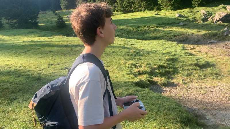 Luis mit Rucksack und Drohnen-Fernbedienung auf einer Almwiese