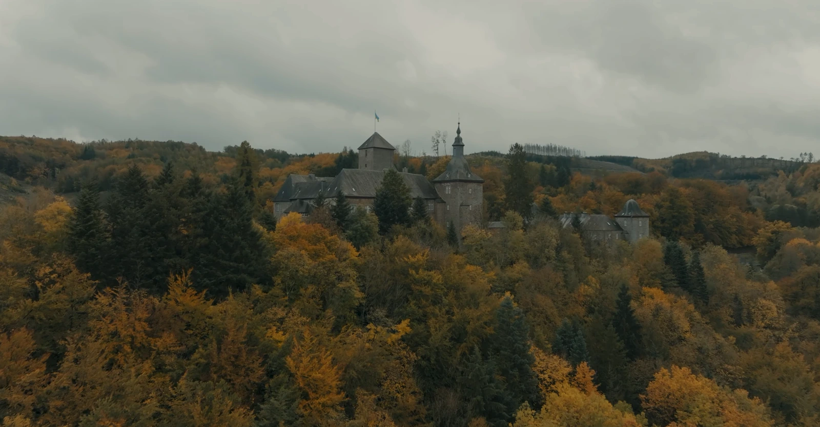 Eine Burg über herbstlichem Wald im Sauerland unter grauem Himmel