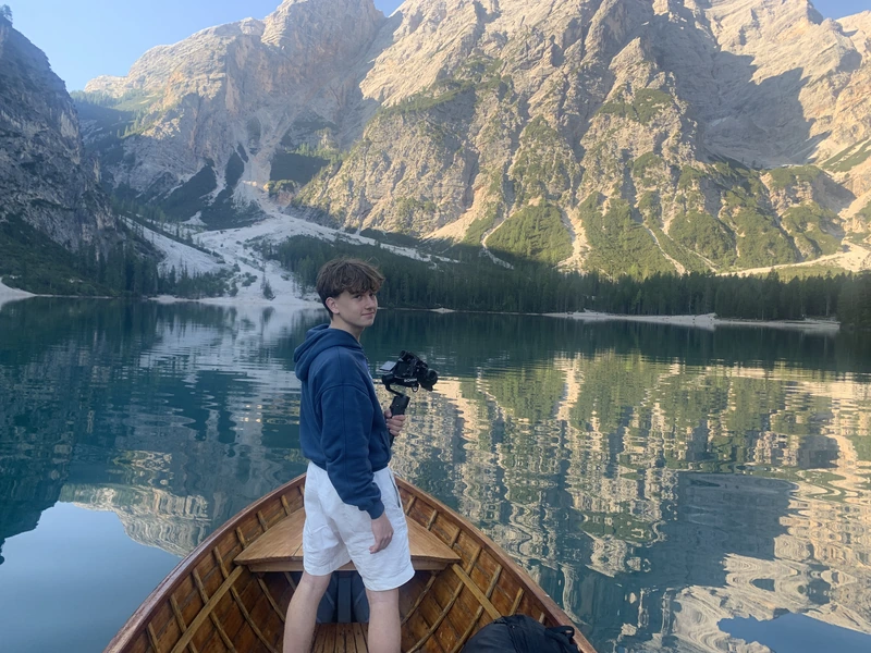 Luis filmt vom Bug eines Ruderboots auf einem Bergsee vor Felswänden