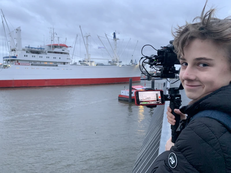 Luis mit Kamera am Gimbal im Hamburger Hafen, dahinter ein Museumsschiff