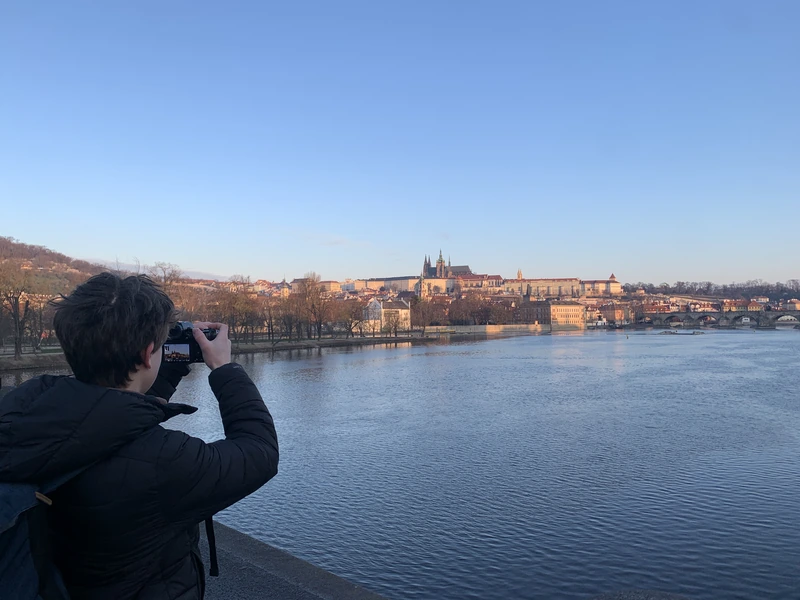 Luis fotografiert am Flussufer, gegenüber eine Altstadt